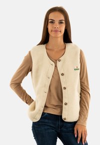 Gilet in pile di colore crema, con bottoni frontali, collo rotondo e dettagli a toppa. Abbinato a una maglietta a maniche lunghe beige.