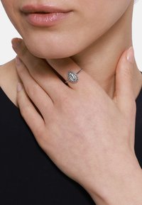 Anello d'argento con una pietra ovale incisa e una superficie texturizzata, montato su una sottile fascia, indossato sulla mano di una persona. Pelle liscia visibile.