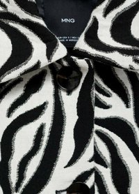 Zwart-witte gestreepte shirt met een kraag, grote zwarte knoppen en een textiel met gestructureerde, draailijnen. Label zichtbaar aan de binnenkant.