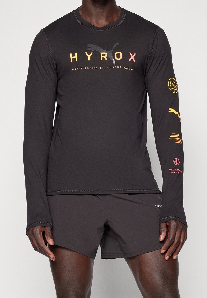 Maglietta atletica nera a maniche lunghe con grafiche del logo giallo e rosso, abbinata a pantaloni corti neri. Design leggero e aderente con cuciture piatte.