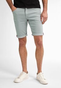 Shorts di cotone grigio chiaro con risvolti, dotati di tasche frontali, abbinati a sneakers bianche e una t-shirt nera.