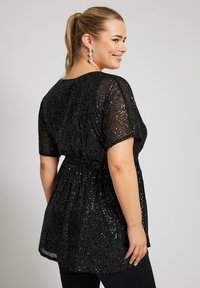 Top nero con paillettes, maniche corte, vestibilità comoda e vita elastica. Texture trasparente con dettagli luccicanti, abbinato a pantaloni neri.
