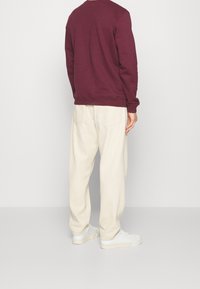 Burgundowa bawełniana bluza z długimi rękawami, okrągłym dekoltem i ściągaczami przy mankietach, zestawiona z kremowymi spodniami o szerokich nogawkach oraz białymi tenisówkami.