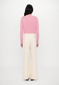 Pink knitted sweater with shoulder details, paired with wide-leg cream pants featuring side pockets. Smooth texture, relaxed fit.