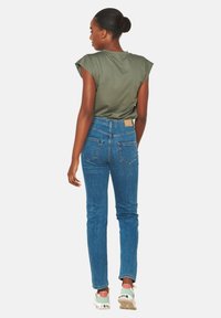 Žalia trumpomis rankovėmis marškiniai, derinami su aukštu liemeniu mėlyniais džinsais, kuriuose yra užpakalinės kišenės ir šviesiai ruda odinė etikete ant liemens.