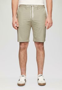 Bermudas beige con un patrón texturizado, cintura elástica y cordón ajustable. Combinadas con zapatillas blancas y marrones.