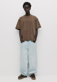 Barna, oversized, rövid ujjú póló, világoskék, laza farmernadrág és fekete cipő barna talppal. Minimalista stílus, egyszerű textúrák.