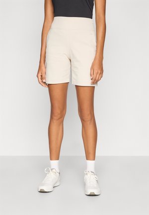 Beige shorts med høyt liv, laget av et glatt materiale, har et rent design og minimal søm. Kombinert med hvite joggesko.