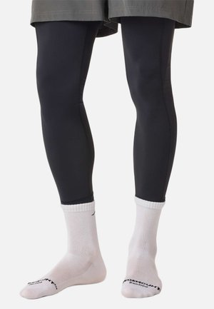 Schwarze Leggings aus elastischem Material mit glatter Textur und figurbetontem Schnitt. Kombiniert mit weißen Sportkniestrümpfen.
