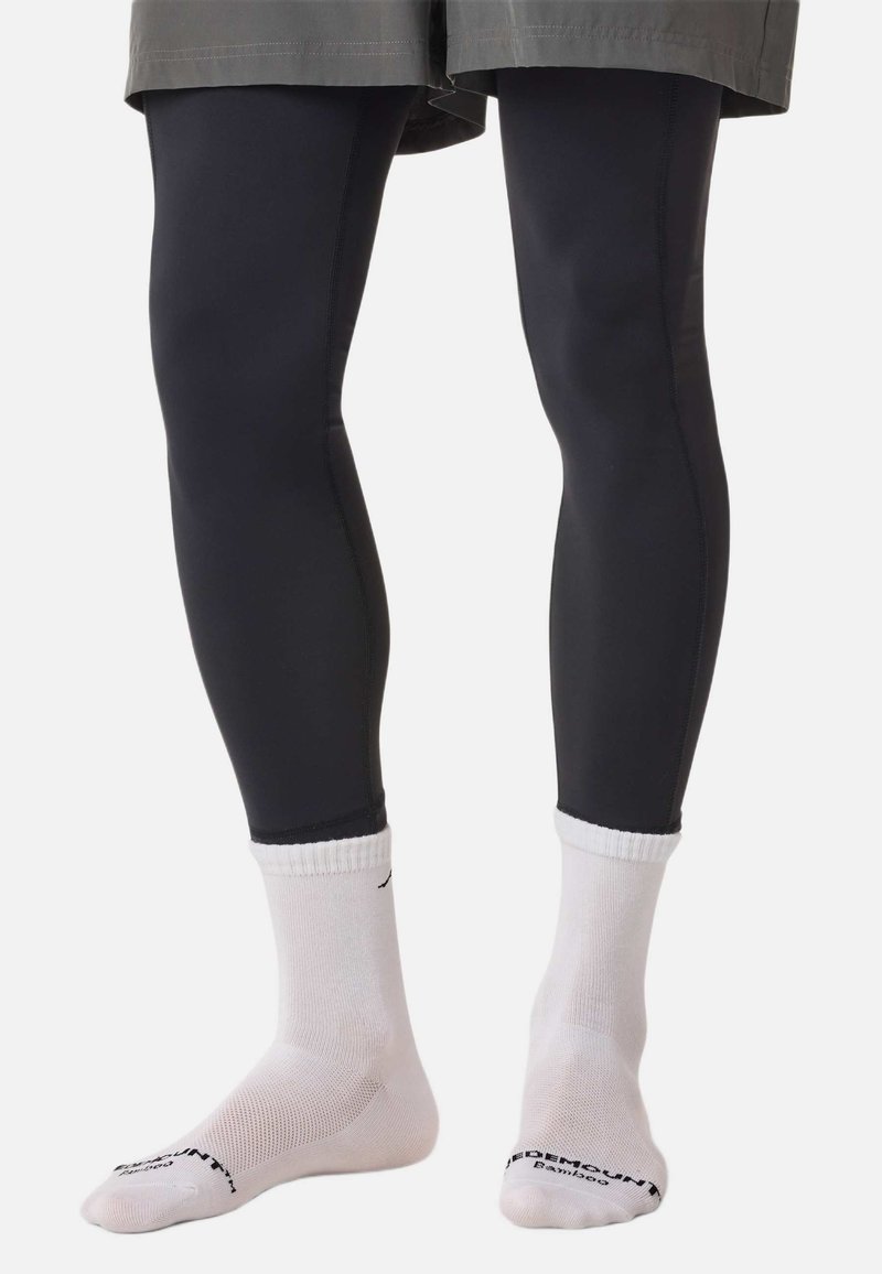 Leggings noirs en matière extensible, présentant une texture lisse et une coupe ajustée. Associés à des chaussettes blanches montantes.