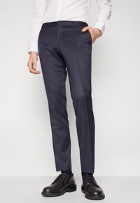 Navy dress pants made from smooth fabric, featuring tapered legs, side pockets, and a flat front design, worn with black shoes.