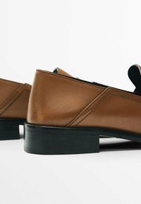 Chaussures en cuir marron à talon bas avec semelles noires et coutures visibles, photographiées sur fond blanc uni.