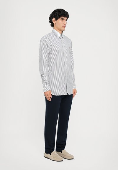 Chemise à manches longues avec des rayures étroites bleu marine et blanches, un col, associée à un pantalon sombre et des mocassins de couleur claire.
