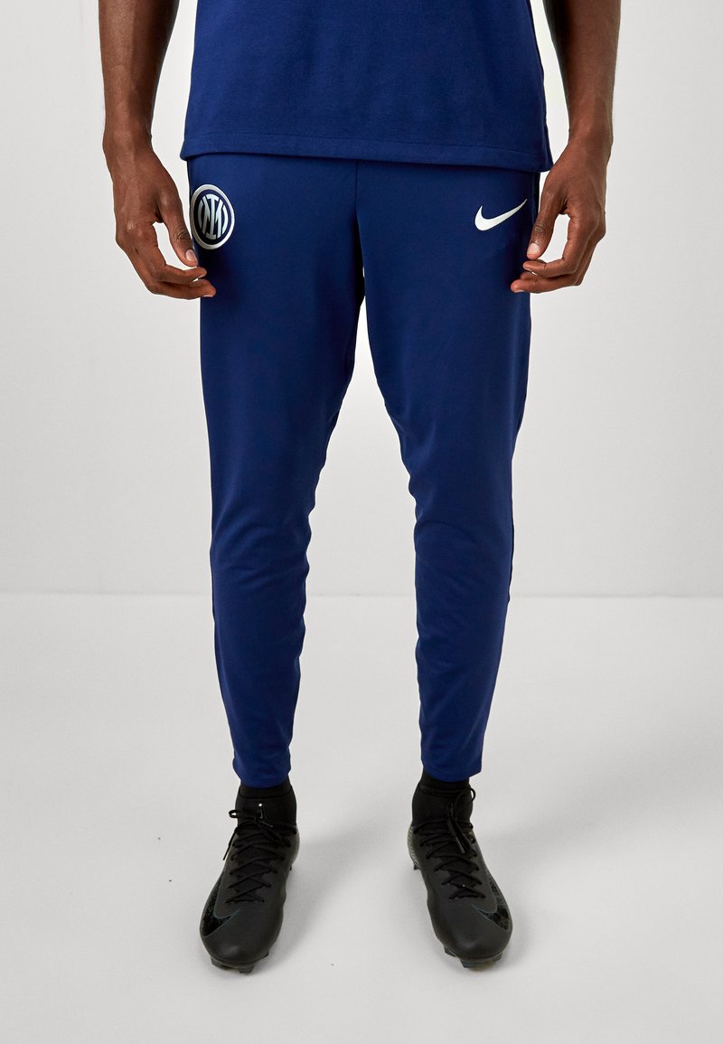 Nike bukser i marineblå polyester, tætsiddende pasform med hvide logo-detaljer; glat tekstur, elastisk talje, velegnet til sport eller casual brug.