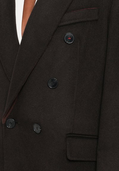 Dubbelgebreide bruine wollen blazer met zwarte plastic knopen, met opgestikte revers en een subtiele rode stikselaccent op een zak.