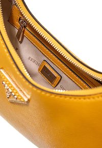 Interno di una borsa gialla con rivestimento di tessuto liscio e una toppa con logo, scomparto con zip e accessori in oro.