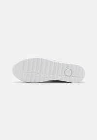Semelle de sneaker en caoutchouc blanc avec des motifs de relief texturés, présentant une forme arrondie et un détail logo circulaire près du talon.