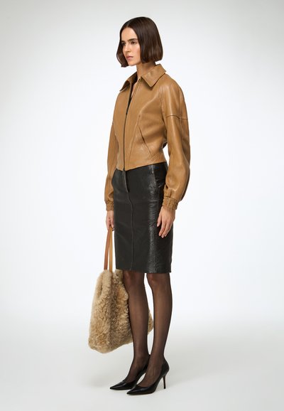 Barna bőr rövidített dzseki gallérral, fekete struktúrált ceruzaszoknyával, fekete hegyes orrú magassarkúval és világosbarna szőrös táskával párosítva.