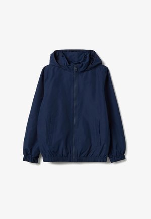 Chaqueta ligera de color azul marino con capucha, cremallera frontal, puños elásticos y dos bolsillos laterales con cintura fruncida.