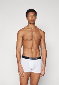 White boxer briefs with a black elastic waistband featuring "bruno banani" logo. Smooth texture, fitted design, and mid-thigh length.