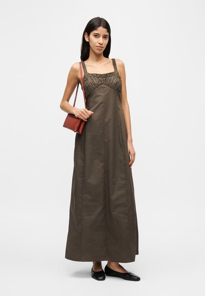 Μάξι φόρεμα σε ελιά ύφασμα με σχέδιο μαζεμένου μπούστου, τετράγωνη λαιμόκοψη και ρυθμιζόμενους ιμάντες; συνδυασμένο με μικρή κόκκινη τσάντα και μαύρα φλατ παπούτσια.