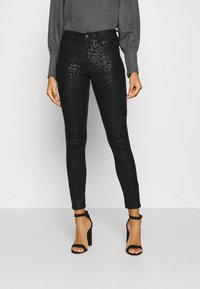 Black faux leather skinny pants featuring a subtle leopard print pattern, with a high waist and ankle-length design. Paired with black heels.