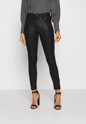 Pantalons skinny en simili cuir noir avec un motif léopard subtil, taille haute et longueur cheville. Assortis avec des talons noirs.