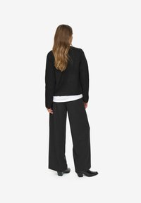 Black knitted sweater with long sleeves, paired with high-waisted, wide-leg black trousers. Black heeled boots complete the look.