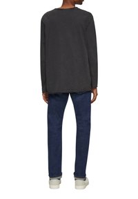 Langsleeve, donkergrijze T-shirt met een ronde hals. De stof lijkt enigszins textuur te hebben. Gecombineerd met blauwe jeans en lichtgekleurde schoenen.