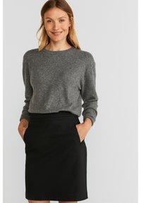 Pull en laine gris à col rond, associé à une jupe noire ajustée avec deux poches latérales. Texture lisse, design minimaliste.
