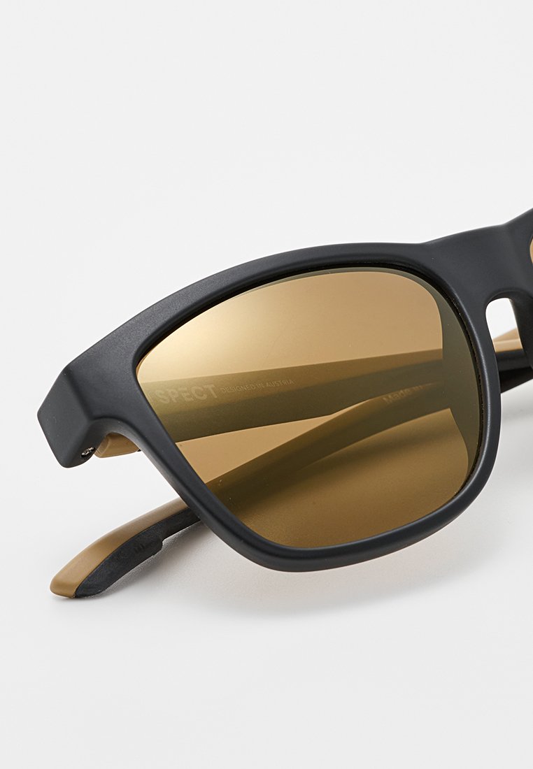 Czarne okulary przeciwsłoneczne z brązowymi szkiełkami, matowe wykończenie, okrągły kształt i subtelne logo na wewnętrznej części zausznika. Gumowane końcówki zauszników dla komfortu.