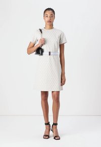 Robe gris clair avec un motif géométrique, manches courtes, cintrée à la taille avec une ceinture rayée, associée à un petit sac à main noir et des talons.