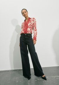 Červená a bílá květovaná košile s dlouhým rukávem, černé džíny s širokými nohavicemi a černé boty na podpatku se špičatou špičkou. Hladká textura, přiléhavá v pase, volný střih.
