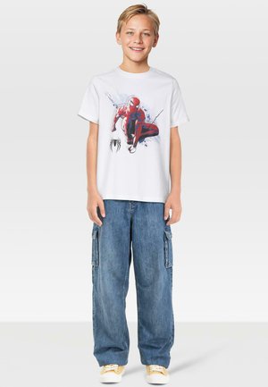 Biała bawełniana koszulka z grafiką Spider-Mana, zestawiona z luźnymi niebieskimi dżinsowymi spodniami typu cargo z wieloma kieszeniami. Do kompletu casualowe obuwie.