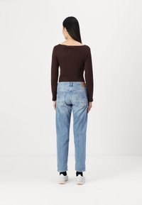 Top marrón de manga larga combinado con unos vaqueros de corte suelto en azul claro, con un aspecto desgastado y detalles de costura sutiles. Zapatillas blancas completan el conjunto.