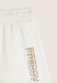 Pantalones de chándal blancos de algodón con cintura elástica y un brillante logo dorado "Freddy" adornado con pequeños remaches en la pierna izquierda.