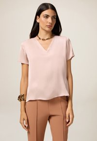 Blusa rosa a maniche corte con scollatura a V in tessuto morbido, caratterizzata da una vestibilità comoda e orlo curvo, abbinata a pantaloni beige a vita alta.