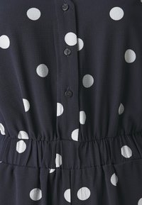 Navy dress with white polka dots, featuring buttons down the front and an elastic waist. Soft, textured fabric with a gathered waistline.