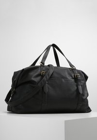 Borsa da viaggio in pelle nera con due manici superiori e una tracolla staccabile. Caratterizzata da accessori in tonalità oro, superficie testurizzata e chiusura con zip.