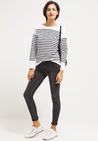Stribet langærmet top i hvid og sort, parret med sorte skinny jeans. Modellen har hvide sneakers og en sort taske på.