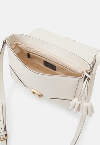 Kermansävyinen nahkalaukku, jossa hienovarainen kohokuvioitu kuvio, kullanväriset metalliosat ja tilava sisätila, jossa on vetoketjutasku ja logolla varustettu tunniste.