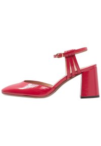Escarpin en cuir verni rouge avec un bout pointu, une bride au cheville et un design à découpes verticales. Il dispose d'un talon large pour plus de stabilité.