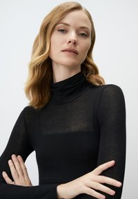 Schwarzes Rollkragenoberteil mit langen Ärmeln, aus leichtem, leicht durchscheinendem Stoff. Einfaches Design, glatte Textur und taillierte Passform.