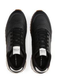 Sneaker nere con tomaia in pelle perforata, design con lacci, suola in gomma bianca e marrone, e etichetta con logo sulla linguetta. Stile minimalista.