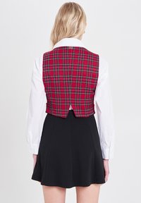 Czerwono-zielona kamizelka w kratę z białą koszulą pod spodem, w połączeniu z czarną spódnicą typu skater. Posiada dopasowany krój i rozporek z tyłu.