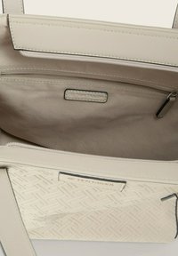 Beige Tragetasche mit gewebter Textur auf der unteren Hälfte, ausgestattet mit einer Reißverschluss-Innentasche und einem Markenetikett. Glattes synthetisches Material.