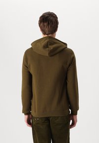 Sudadera con capucha de color verde oliva, hecha de una tela suave, con un bolsillo tipo canguro, puños acanalados y un diseño de corte relajado.