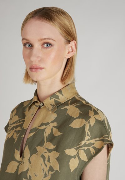 Blusa verde con motivo floreale beige, dotata di colletto, maniche corte e dettaglio a forma di dente di chiusura. Tessuto dal tocco morbido.