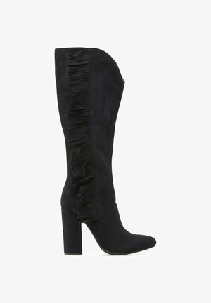 Bota negra de ante hasta la rodilla con tacón grueso y detalle de flecos que recorren verticalmente el lateral exterior.