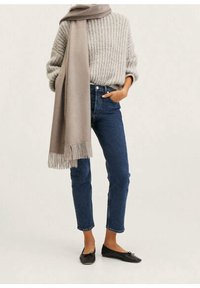 Pull gris en tricot, écharpe beige à franges, jean taille haute bleu, et mocassins noirs. Textures douces, coupe décontractée, tons naturels.